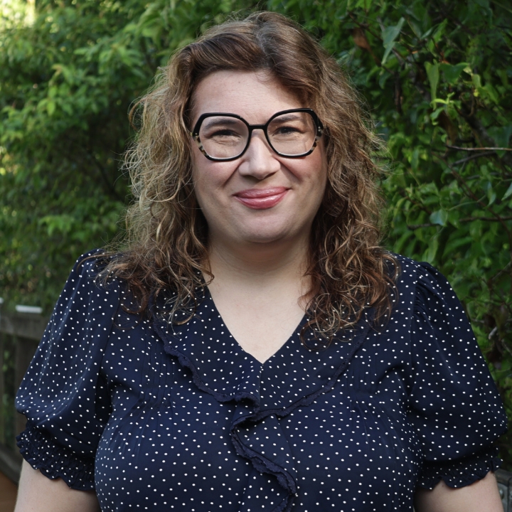 Anastasiya Shirley, Kaleidoscope Adventures team member, smiling outdoors in glasses and a navy polka-dot blouse.
