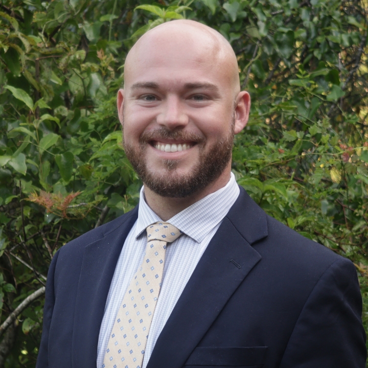 Cameron Parker, Kaleidoscope Adventures team member, smiling outdoors in a navy suit and patterned tie.