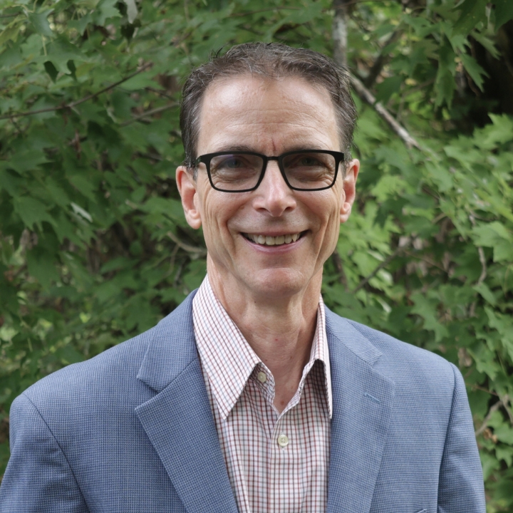 Joseph Hodge, Kaleidoscope Adventures team member, smiling outdoors in glasses and a blue blazer.