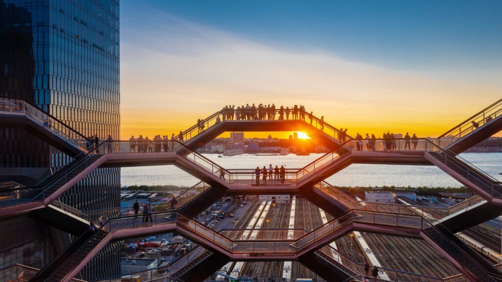 group of people standing on the vessel at Hudson Yards with the sun going down behind them over the river