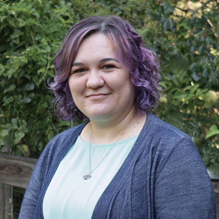Genevieve Jimenez, Kaleidoscope Adventures team member, smiling outdoors with purple hair and a light blue top.
