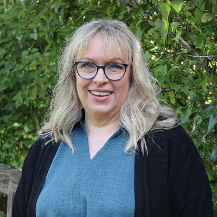 Gayle Sembroff, Kaleidoscope Adventures team member, smiling outdoors in glasses, a blue blouse, and a black cardigan.