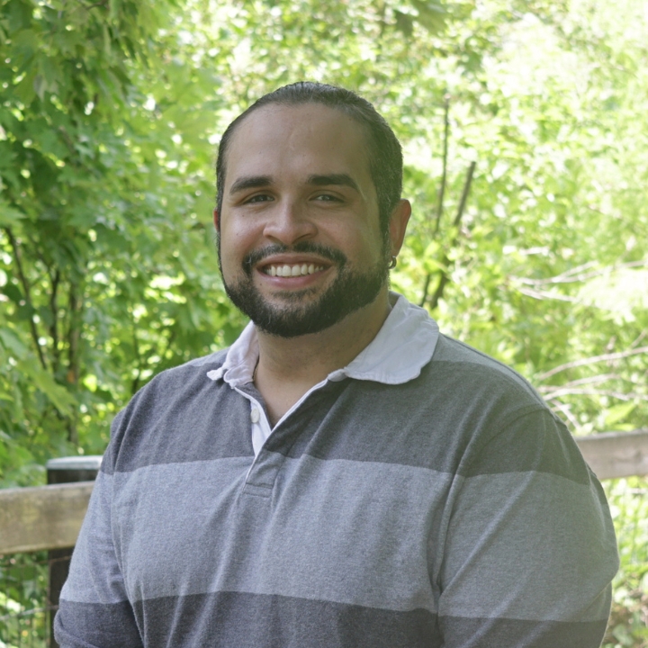Stephen Escobar, Kaleidoscope Adventures team member, smiling outdoors in a gray striped polo shirt.