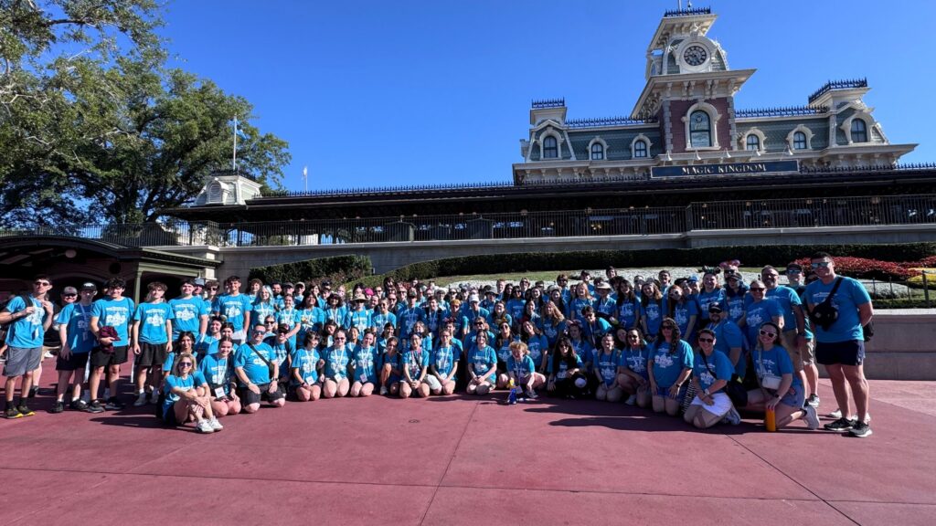 a large group of older teens in matching blue t-shirts posing or a photo outside the entrance to Walt Disney World's Magic Kingdom