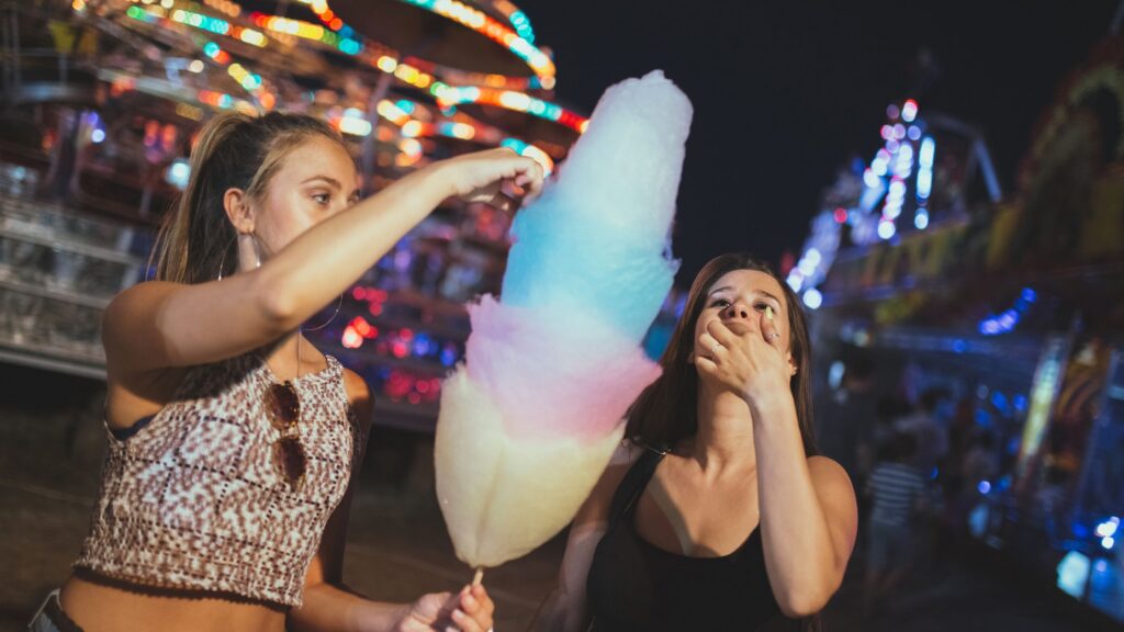 2 older teen girls enjoying cotton candy at a theme park at night