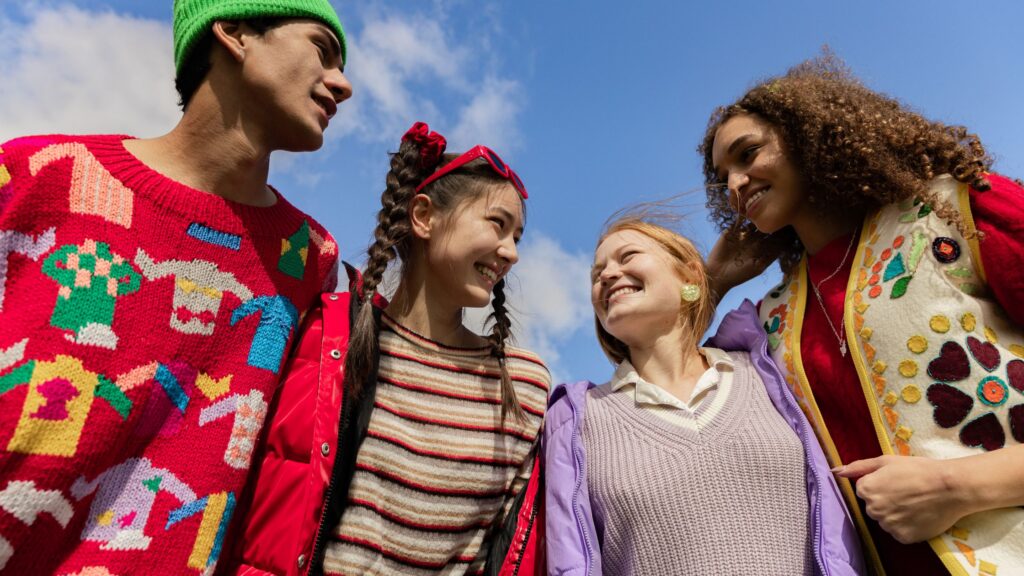 group of 4 older, multi-ethnic teens in colorful sweaters smiling