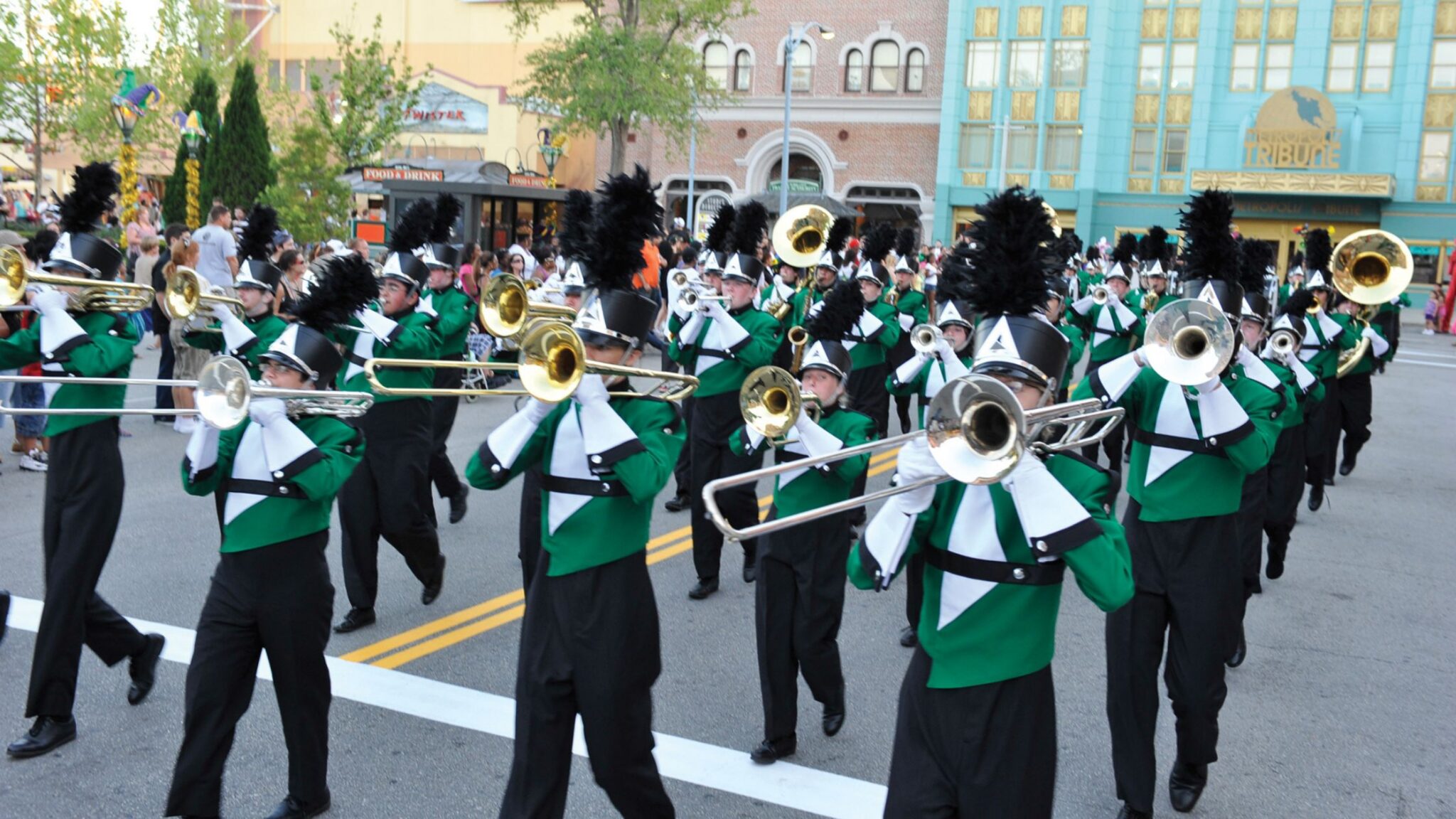 high school band students in green uniforms marching on a theme park street