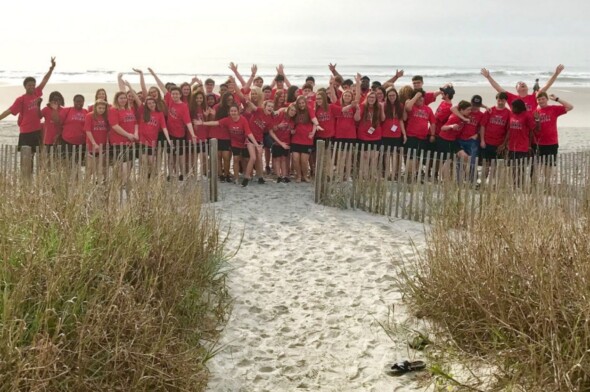 large group of teens in red tshirts on a beach smiling for a photo